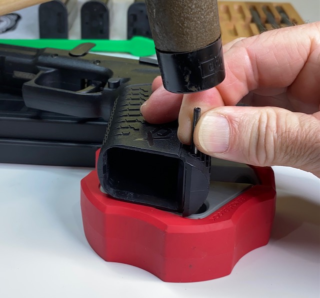 Carefully line up the roll pin with the hole and tap it back into the grip