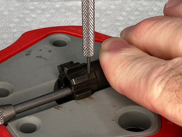 Use a larger punch to press the Ejector Plunger into the bolt until the smaller punch can be pushed far enough into the hole to capture the notch